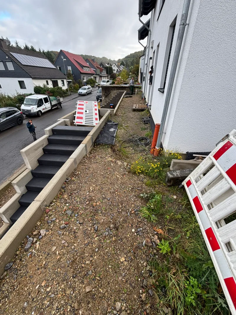 Abgegrabener Hang neben einer Außentreppe an einem weißen Neubau, am Rand eine Absperrung