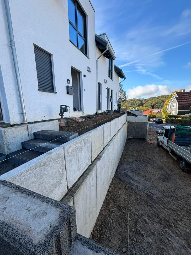 Betonwinkelsteine vor weißen Neubauten, davor eine frisch abgezogene Erdfläche