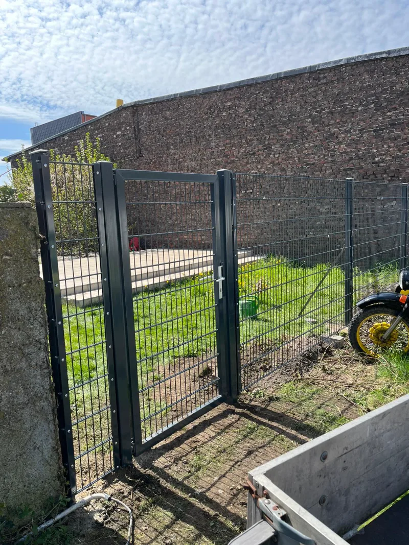 Neues dunkles Gartentor in einem Stabmattenzaun, dahinter eine Rasenfläche