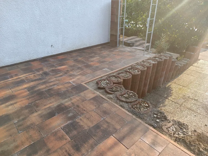 Terrasse aus rotbraunem Klinkerpflaster, seitlich eine Beetkante aus runden Palisaden